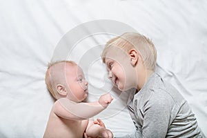 Baby and smiling older brother are lying on the bed. They play, communicate and interact. Top view