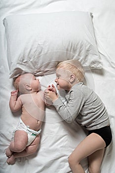 Baby and smiling older brother are lying on the bed. They play, communicate and interact. Top view