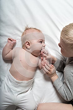 Baby and smiling older brother are lying on the bed. They play, communicate and interact. Top view