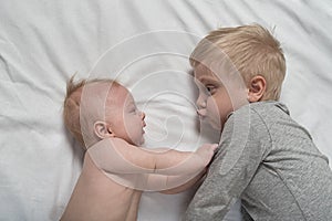 Baby and smiling older brother are lying on the bed. They play, funny and interact. Top view