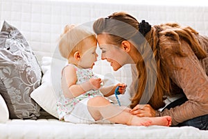 Baby with soother and young mom playing on divan