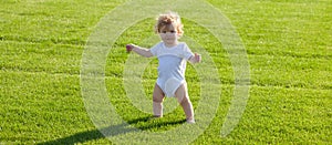Baby on spring grass field, banner. Baby standing barefoot on the green lawn. Healthy child.