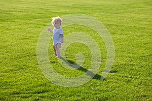 Baby standing barefoot on the green lawn.