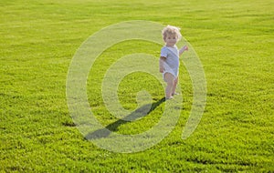 Baby standing barefoot on the green lawn.