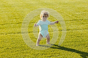 Baby standing barefoot on the green lawn. Healthy child.
