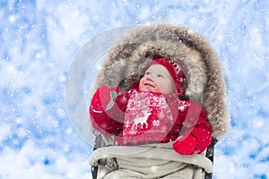 Baby in stroller in winter park with snow