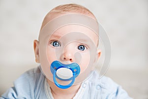 Baby sucking Pacifier looking at Camera. Child with Kids Smoother. Infant Boy Face Portrait with Dummy and Blue big Eyes in white