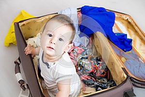 Baby in a suitcase, a journey. A small child got out of the suitcase and looks at you. Packed for vacation in sea resort. The