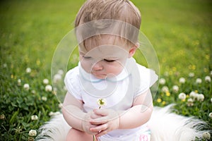 Baby in a Summer flower meadow with a flower in hand