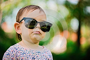 Baby with sunglasses on the green grass background on a sunny day, lifestyle