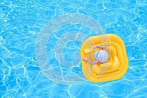 Baby swim in a yellow inflatable raft in a pool of blue water