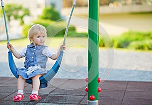 Baby swinging on swing on playground. Side view