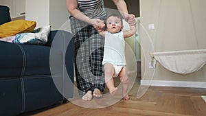 Baby takes the first steps to learn. Happy family kid dream concept light. Mom teaches baby newborn to walk and take