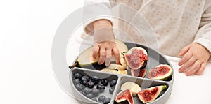 Baby taking fruits and berries from silicone plate on white background, close-up shot. Child self nutrition concept