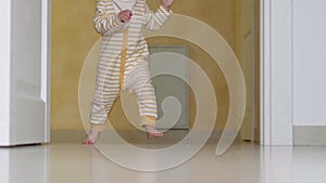 Baby taking making first steps . Little child girl or boy running walking on white floor at home. Barefoot legs kid on