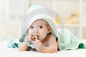 Baby with teether in mouth under bathing towel at nursery