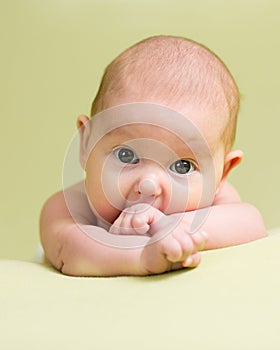 Baby teething. Infant kid sucks fingers lying on belly in nursery