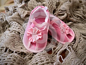 Baby tiny delicate pink booties with a flower bow. A close-up photo on the background of a beige soft knitted plaid. Shoes for a