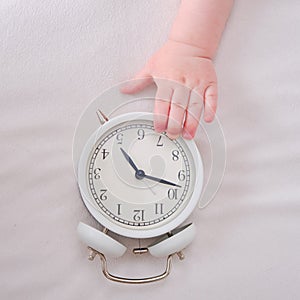 Baby toddler boy holds an alarm clock in his hand. Child with a white al