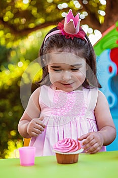 Baby toddler girl in outdoor party at garden, happy and smiling at cupcake with sweet tooth expression photo