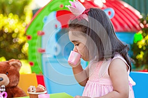 Baby toddler girl playing in outdoor tea party drinking from cup with best friend Teddy Bear