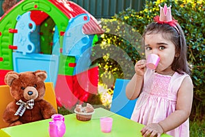 Baby toddler girl playing in outdoor tea party drinking from cup with best friend Teddy Bear