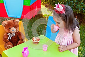 Baby toddler girl playing in outdoor tea party drinking from cup with best friend Teddy Bear