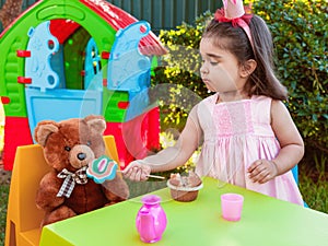 Baby toddler girl playing in outdoor tea party feeding her best friend bff Teddy Bear with a tasty lollipop
