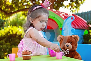 Baby toddler girl playing in outdoor tea party serving her best friend Teddy Bear with candy gummy