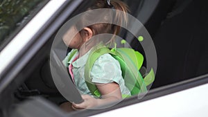 Baby toddler girl sitting on front seat of car with steering wheel. Back to school ride