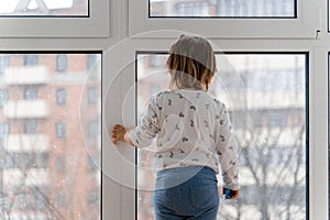 Baby toddler girl standing near the window and watching outside. Indoor play