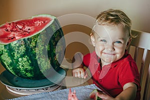 Baby Todler sit at a table near a large watermelon and smiles. selective focus