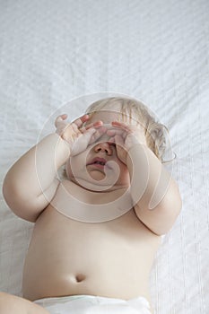 Baby touching eyes on white bed