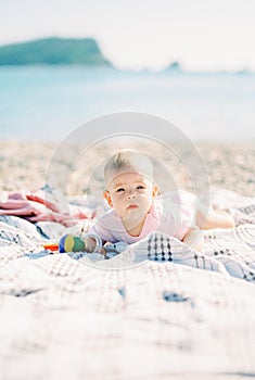 Baby with a toy in his hands lies on his tummy on a beach
