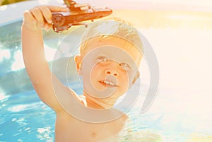 Baby with toy plane in swimming pool. Little boy learning to swim in outdoor pool.