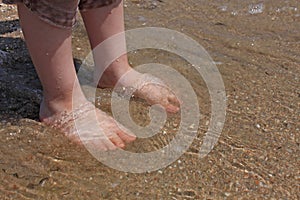 A baby try to step in to the sea water at the first time in a sunny day. With blurry sea background
