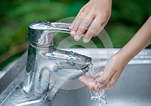 Baby try to turn off water faucet but water still leak. A child`s hand turning off the tap. Save water. World Water Monitoring Da