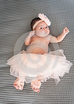 baby in tutu and ballet shoes reclining on a blanket looking at the camera
