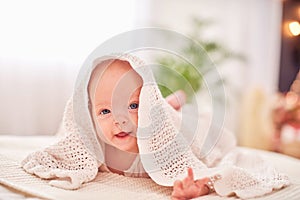 Baby under the towel. a cheerful little child looks out from under the blanket and smiles funny. lying on his stomach on their own