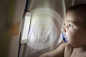 Baby watching a lullaby cartoons with mobile phone on the crib