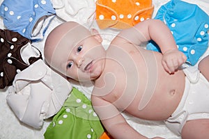 Baby Wearing a Cloth Diaper Surrounded by a Rainbow of Cloth Diapers photo