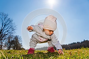 Baby wearing warm beanie hat, sweatshirt and red boots outdoors in rural area discovering nature in spring, sunny day
