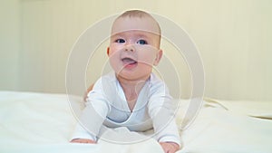 Baby in white clothes lying on paunch on white bed