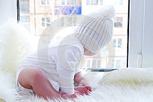 Baby in a white hat sits on a window sill