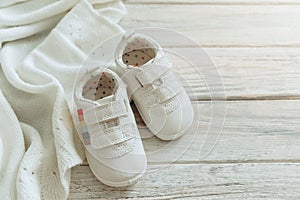 Baby white shoes and warm blanket on wooden background