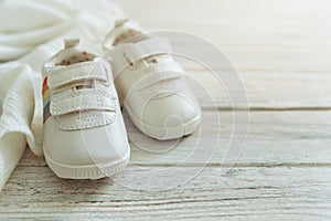 Baby white shoes and warm blanket on wooden background