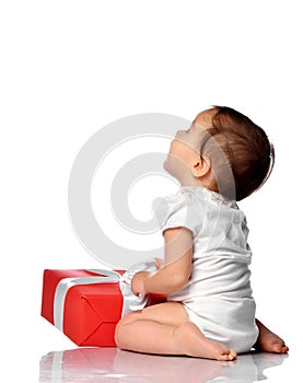 Surprised baby in jumpsuit sitting with gift box looking aside