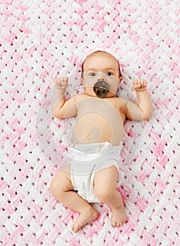 Baby girl in diaper lying with pacifier on blanket
