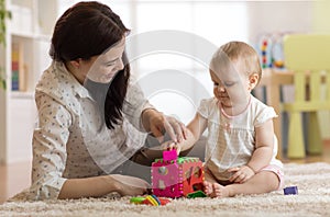 Babysitter and baby playing with toys in nursery