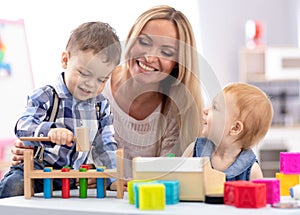 Babysitter and children playing together in nursery or day care centre photo